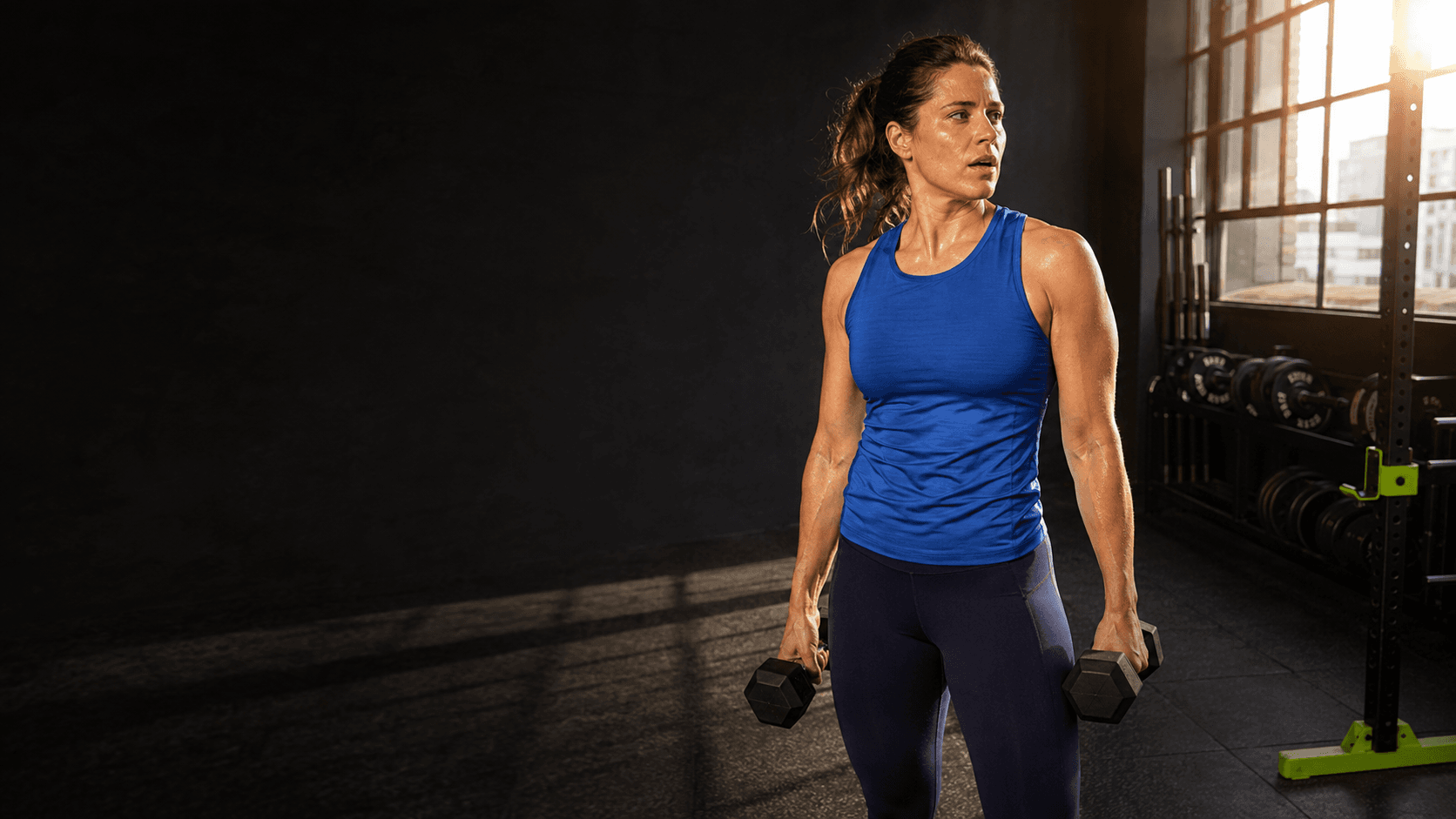 An athlete training with dumbbells in a sunlit gym